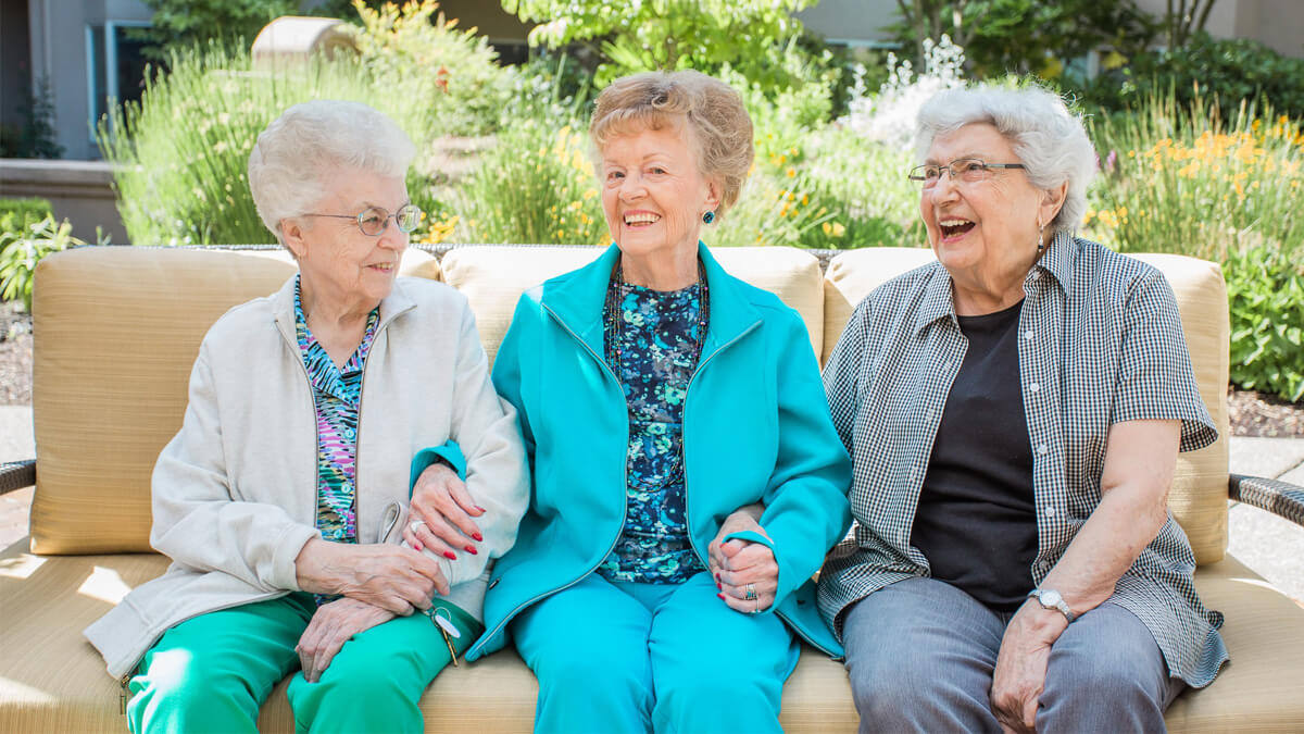 Three residents sitting on an outdoor couch at the Grand Park community
